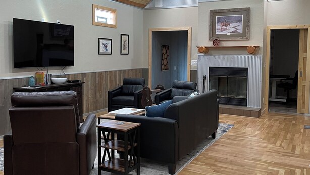A spacious living room with a wooden ceiling, a flat-screen TV, a fireplace, and a large window. - Spacious Convenient Downtown Cody Location (Cody)