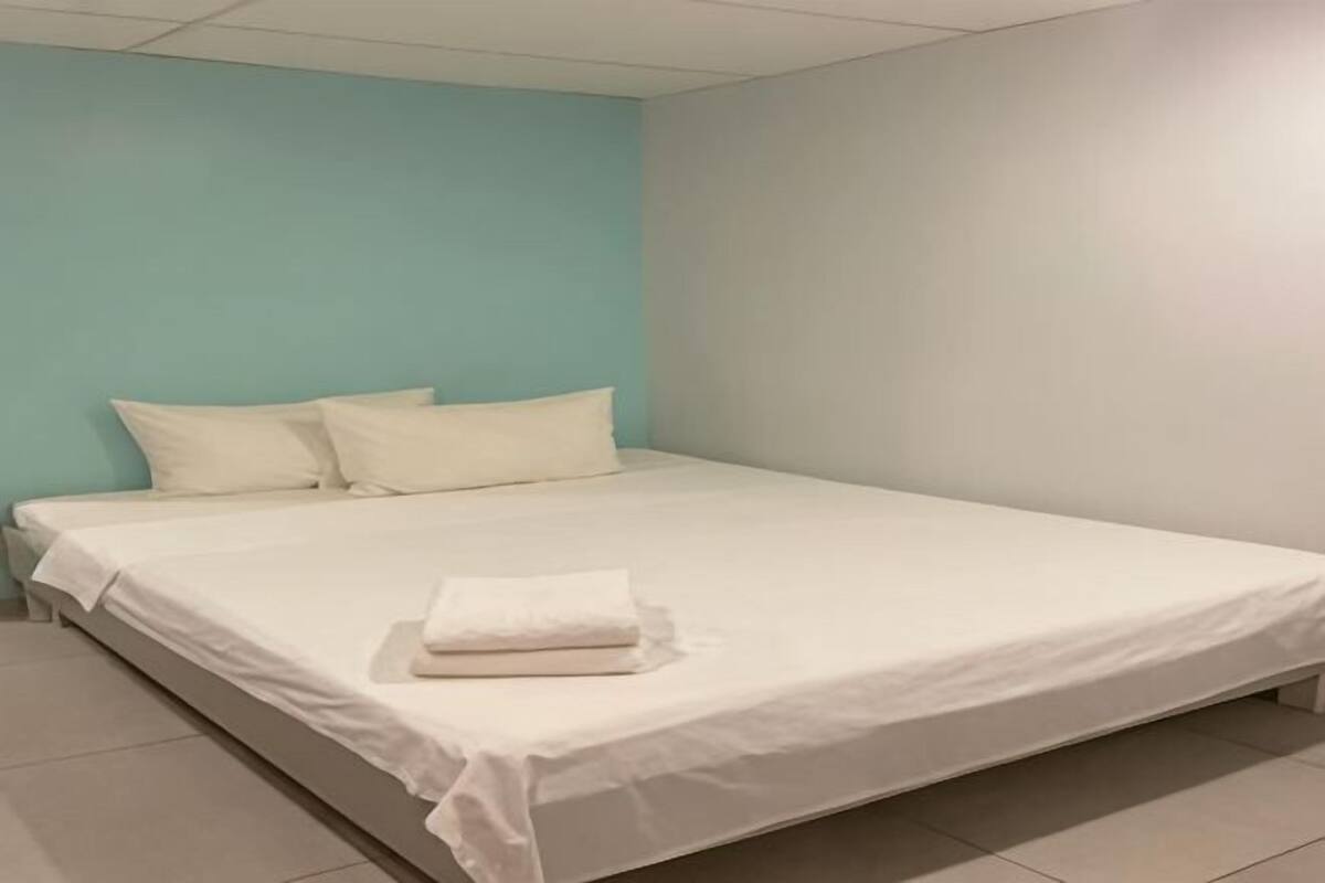 Una cama individual con ropa blanca en una habitación con paredes azul verdosas y blancas.