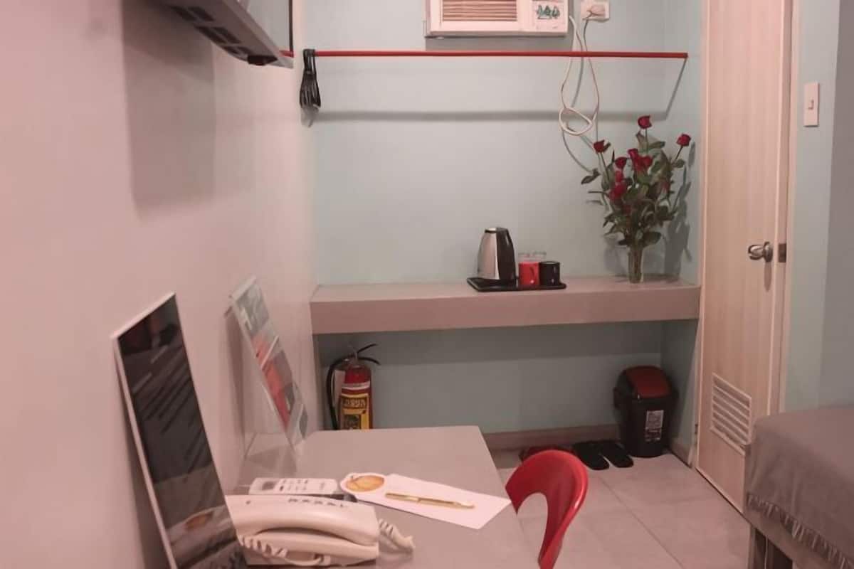 Una habitación pequeña con un escritorio, una silla y una estantería con un florero.