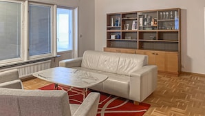 Un salon avec un canapé beige, une petite table basse, un tapis rouge et un meuble en bois doté d’étagères en verre.