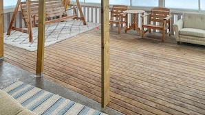 Une terrasse en bois avec une balançoire, une table ronde et des chaises.