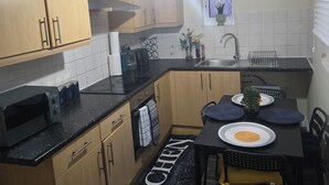 A compact kitchen with wooden cabinets, a microwave, a sink, and a dining area with a table set for two. - A 2beds luxury stylish apartment in queen street Wolverhampton (Featherstone)