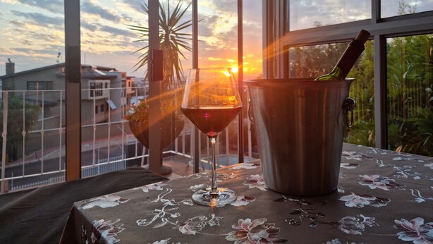 Una mesa con mantel floral, una copa de vino tinto y un recipiente metálico con sacacorchos.