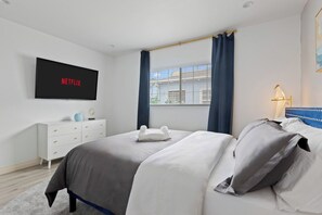 A modern bedroom with a bed, a flat-screen TV mounted on the wall, a dresser, and a window with curtains. - Jacuzzi|PacMan|PS4|Darts|Fireplace|Parking|Grill (Culver City)