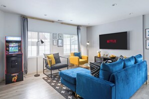 A modern living room with a blue sofa, a yellow armchair, a gaming console, and a TV displaying 'NETFLIX'. - Jacuzzi|PacMan|PS4|Darts|Fireplace|Parking|Grill (Culver City)