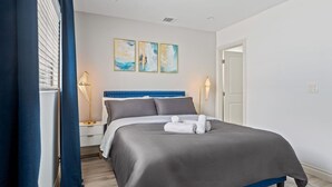 A modern bedroom with a bed, two bedside tables, a nightstand, a blue curtain, and a wall with three paintings. - Jacuzzi, Parking, and Game Night Retreat with PS4 PacMan Darts Grill (Culver City)