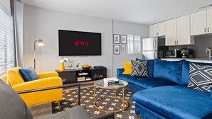 A modern living room with a blue sofa, yellow armchair, and a TV displaying 'NETFLIX'. - Jacuzzi, Parking, and Game Night Retreat with PS4 PacMan Darts Grill (Culver City)