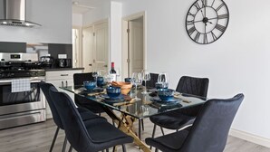 A modern kitchen with stainless steel appliances, a dining area with a glass table and black chairs, and a large wall clock. - Jacuzzi, Parking, and Game Night Retreat with PS4 PacMan Darts Grill (Culver City)