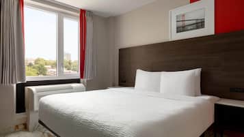 Una habitación de hotel con una cama grande, una mesita de noche, un cuadro enmarcado en la pared y una ventana con cortinas.