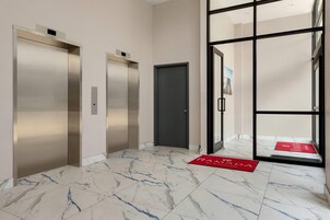 A hallway with two elevators, a door, and a red mat with "RANADA" on it.