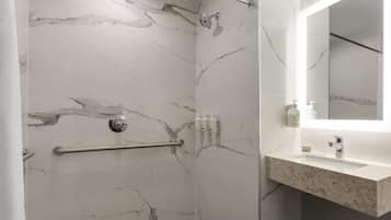 Une salle de bain moderne avec des murs en marbre, une douche équipée d’un pommeau de douche amovible, d’une barre d’appui et d’un meuble-lavabo avec un miroir.