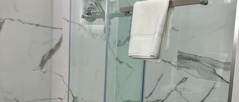 A glass-enclosed shower with marble walls, a towel rack, and toiletries on a shelf.