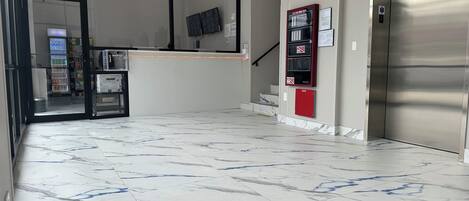 A lobby with a marble floor, a reception desk, a staircase, and an elevator.