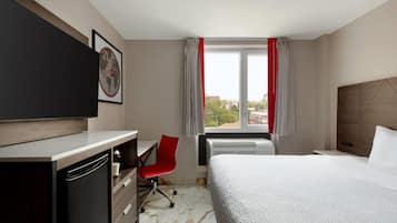 A hotel room with a bed, a desk with a chair, a television, and a window with curtains.
