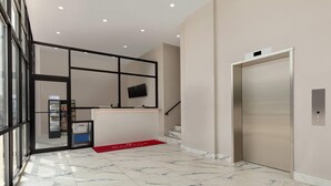 Un hall d’entrée moderne avec un sol en marbre, un comptoir d’accueil, un distributeur automatique et un ascenseur.