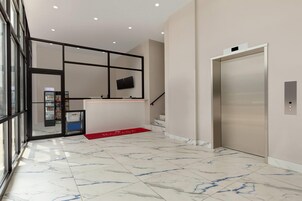 A modern lobby with a marble floor, a reception desk, a vending machine, and an elevator.