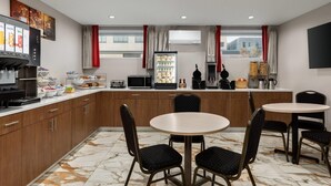 Une cuisine moderne avec un sol en marbre, des meubles en bois, un réfrigérateur, un four à micro-ondes, un grille-pain et une machine à café. On y trouve deux tables rondes accompagnées de chaises.