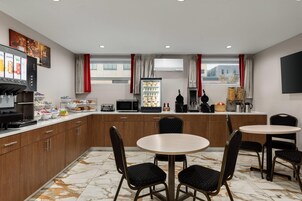 A modern kitchen with marble flooring, wooden cabinets, a refrigerator, microwave, toaster, and a coffee machine. There are two round tables with chairs.