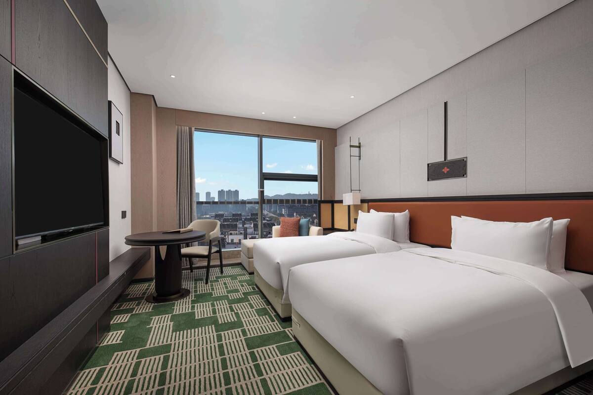 Ein Hotelzimmer mit zwei Betten, einem Fernseher, einem kleinen Tisch und einem Stuhl.