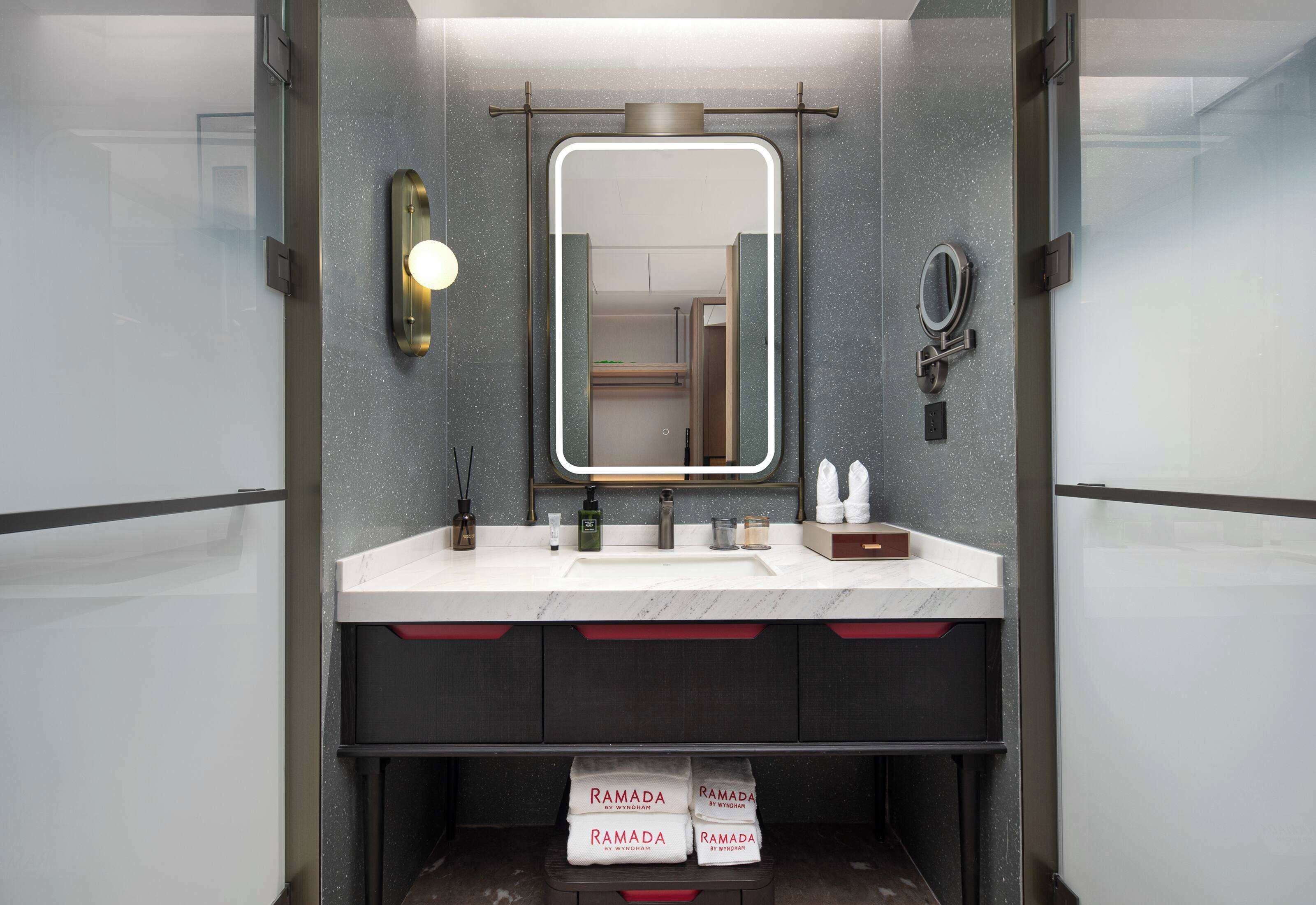 Une salle de bain moderne avec un grand miroir, un lavabo doté d’un distributeur de serviettes et une étagère où sont pliées des serviettes.