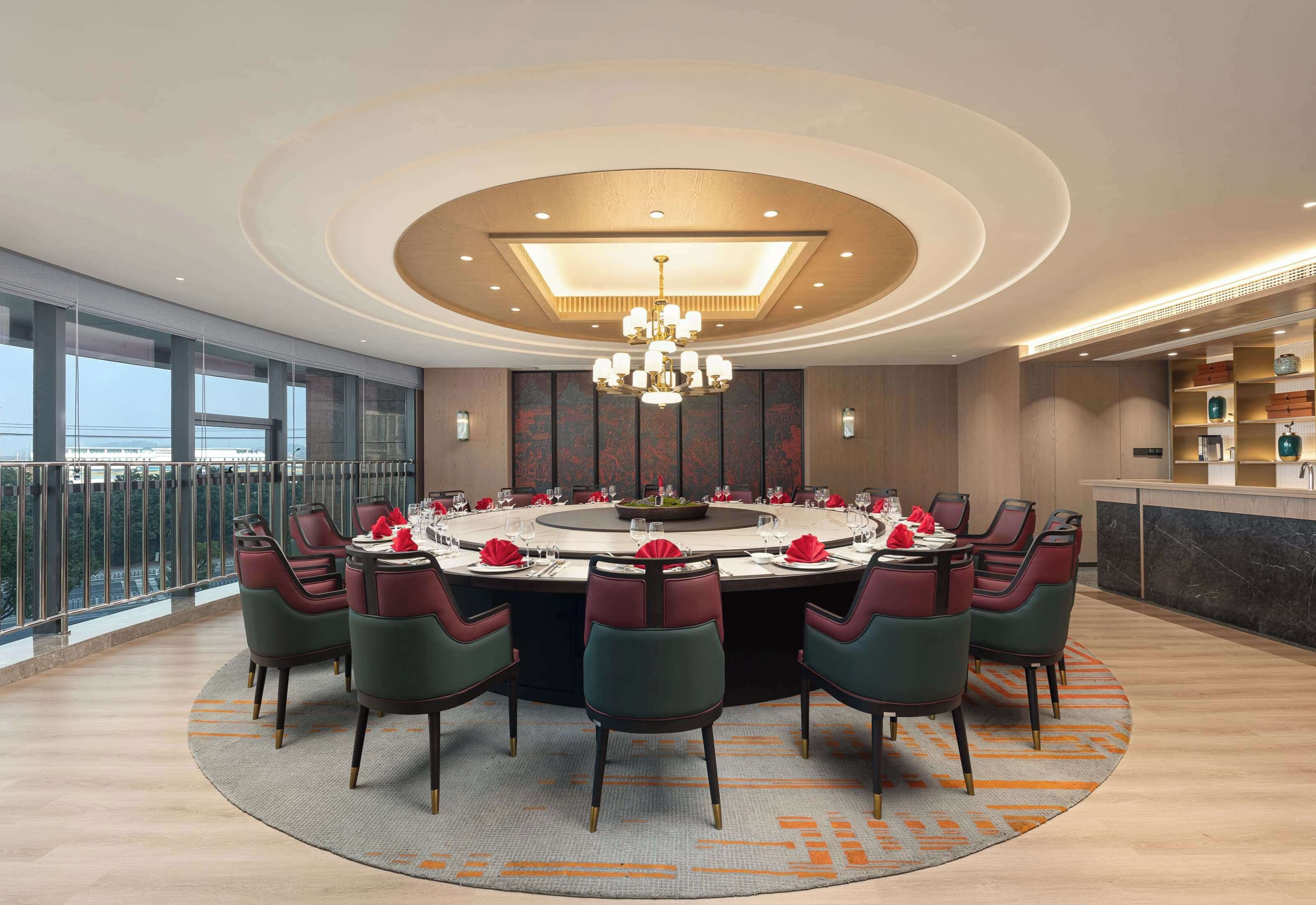 Mesa de jantar redonda com cadeiras, um candelabro e vista da cidade através de grandes janelas.