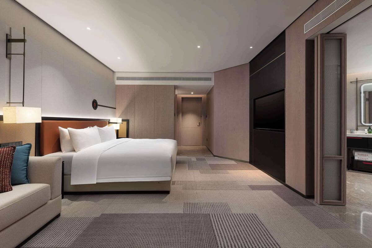 Ein modernes Hotelzimmer mit einem großen Bett, einer Couch, einem Fernseher und einer Minibar.