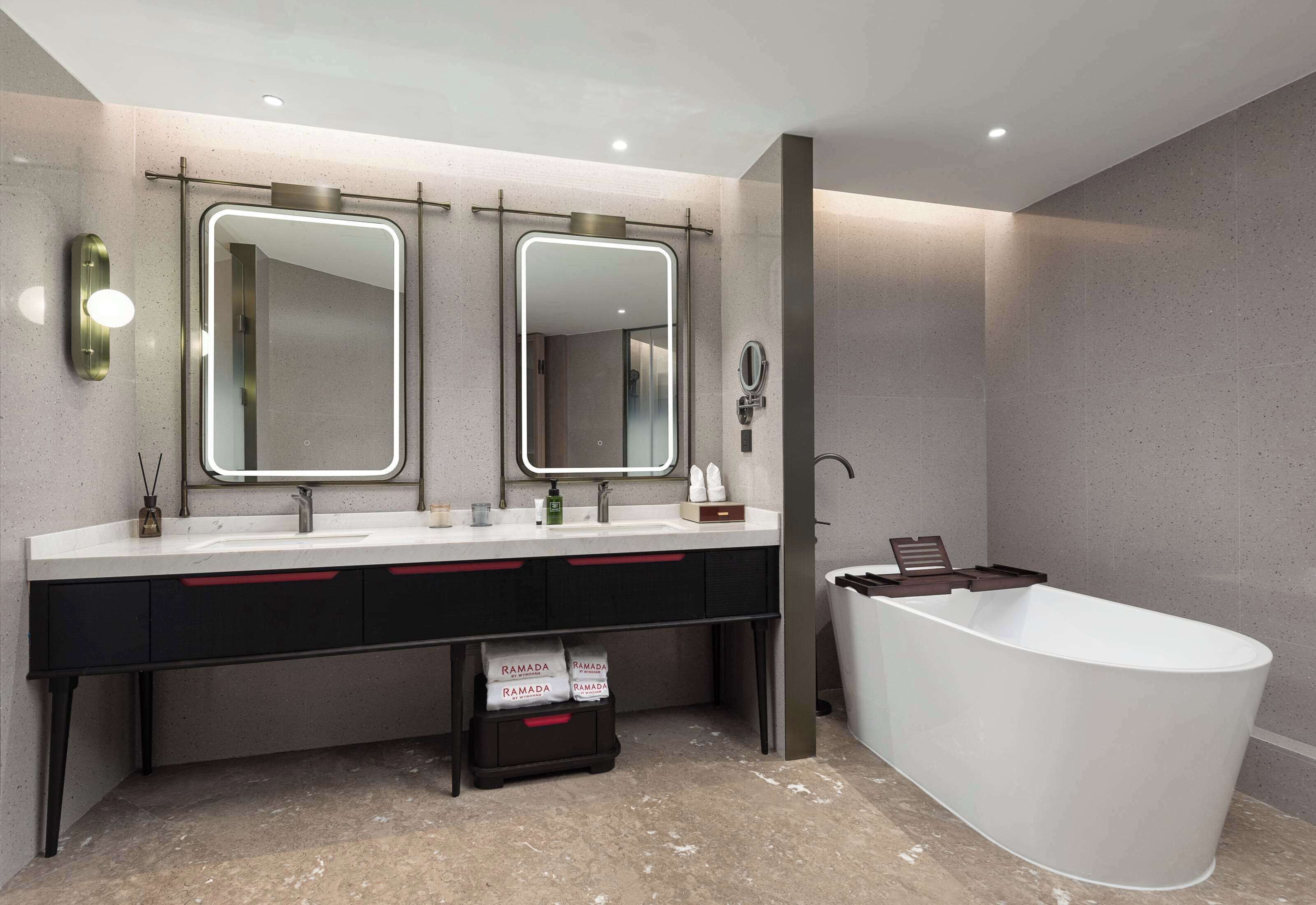 Un baño moderno con una bañera blanca grande, un tocador doble con dos espejos y un lavamanos pequeño.