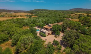 A villa surrounded by dense trees, a swimming pool, and a hilly landscape.