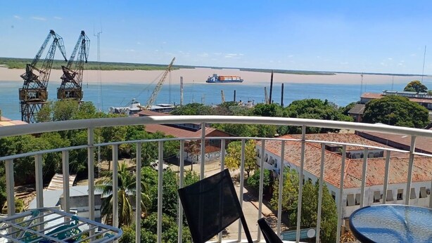 Un balcon avec vue sur une plage, un cargo et des grues industrielles.