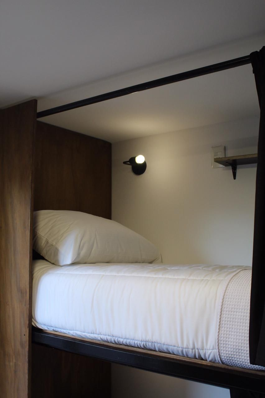 Una cama individual con cabecera, una lámpara de noche y una estantería encima.