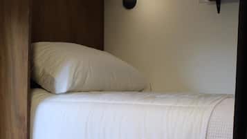 Una cama individual con cabecera, una lámpara de noche y una estantería encima.