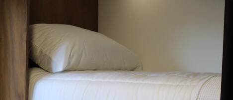 Una cama individual con cabecera, una lámpara de noche y una estantería encima.