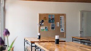 A conference room with a long wooden table, chairs, a bulletin board with papers, and potted plants.
