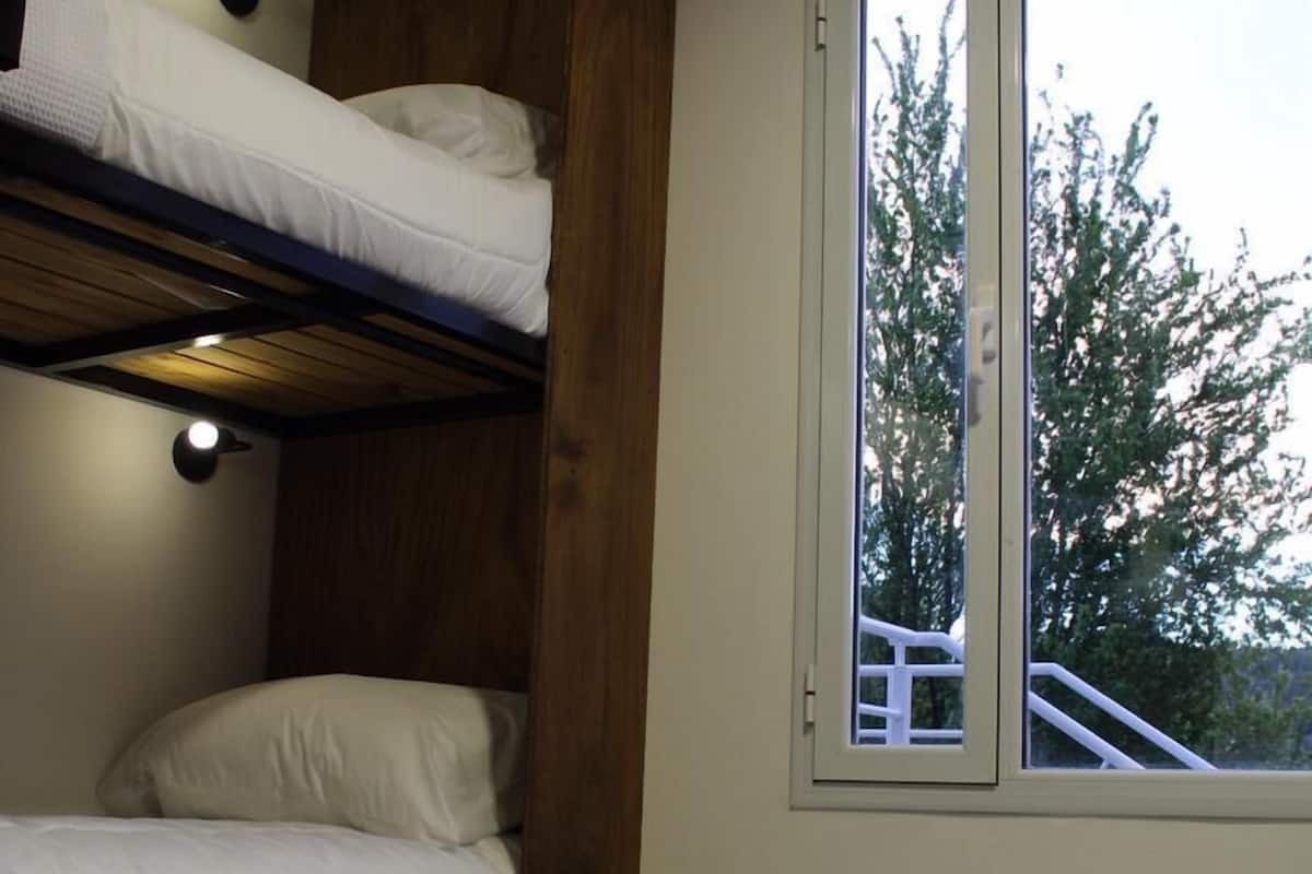 Quarto com beliche, janela grande, paredes de madeira e luminária.