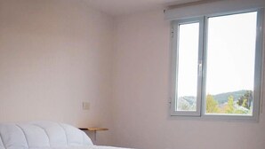 A bedroom with a bed, a nightstand, and a window with a view of the outdoors.