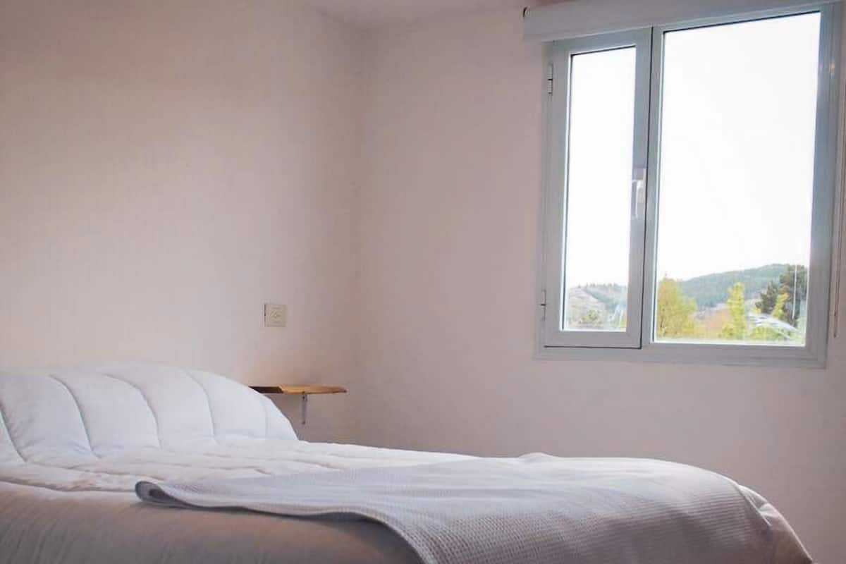 Quarto com uma cama, mesa de cabeceira e janela com vista para o exterior.