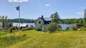 A lakeside cabin with a metal roof, surrounded by lush greenery and a flagpole with a flag. - 2 bedroom gorgeous home in åsensbruk (Åsensbruk)