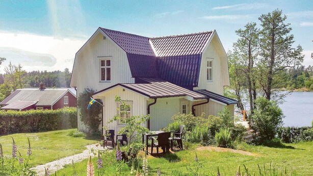 A two-story house with a sloped roof, a porch with chairs, and a flag. - 2 bedroom gorgeous home in åsensbruk (Åsensbruk)