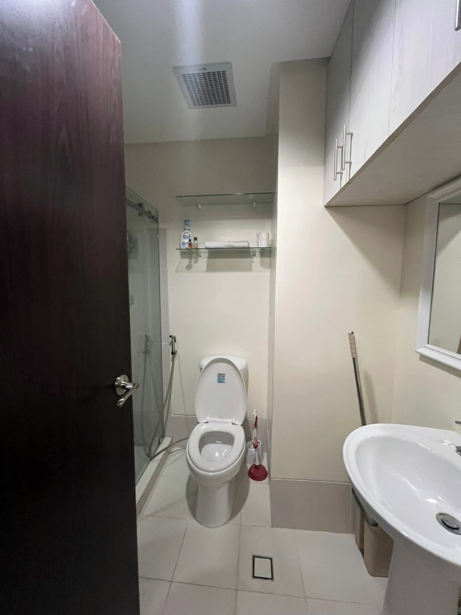 Un baño con inodoro, lavabo, ducha y repisa de vidrio con artículos de aseo.
