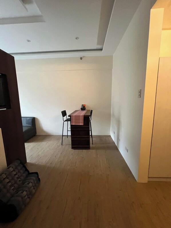 A small, open-plan living space with a dining area, a sofa, and a TV mounted on the wall. - Chelsea Tower 3 (Muntinlupa)