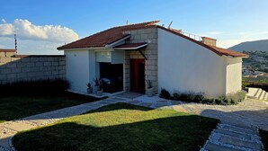 Une maison moderne avec un toit recouvert de tuiles rouges, un mur en pierre et une allée pavée menant à une porte rouge.