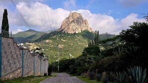 Un sentier pavé mène à une montagne dont le sommet est rocheux, et qui est entourée de verdure et de cactus.