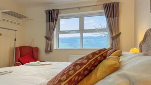 A bedroom with a bed, a red chair, a window with curtains, and a lamp. - 6 bedroom accommodation in Belper (Belper)