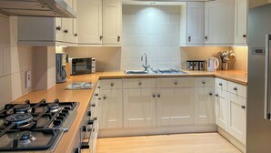 A modern kitchen with white cabinets, a gas stove, a microwave, and a sink. - 6 bedroom accommodation in Belper (Belper)