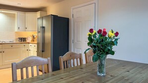A dining area with a wooden table, chairs, a vase with flowers, a refrigerator, and kitchen cabinets. - 6 bedroom accommodation in Belper (Belper)