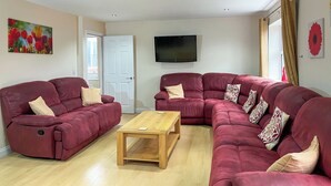 A living room with two red sofas, a wooden coffee table, a flat-screen TV, and a door leading outside. - 6 bedroom accommodation in Belper (Belper)