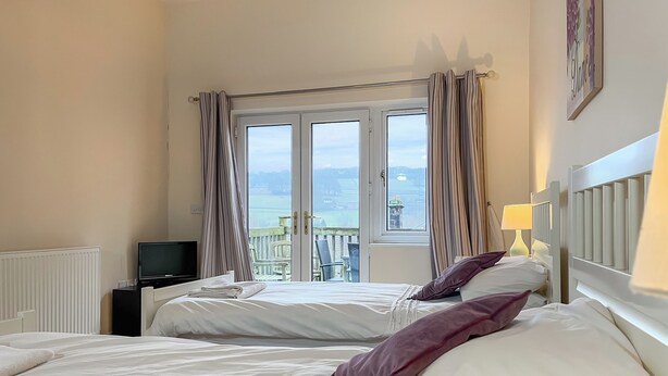 A hotel room with two beds, a television, and a balcony with a view of the sea. - 6 bedroom accommodation in Belper (Belper)