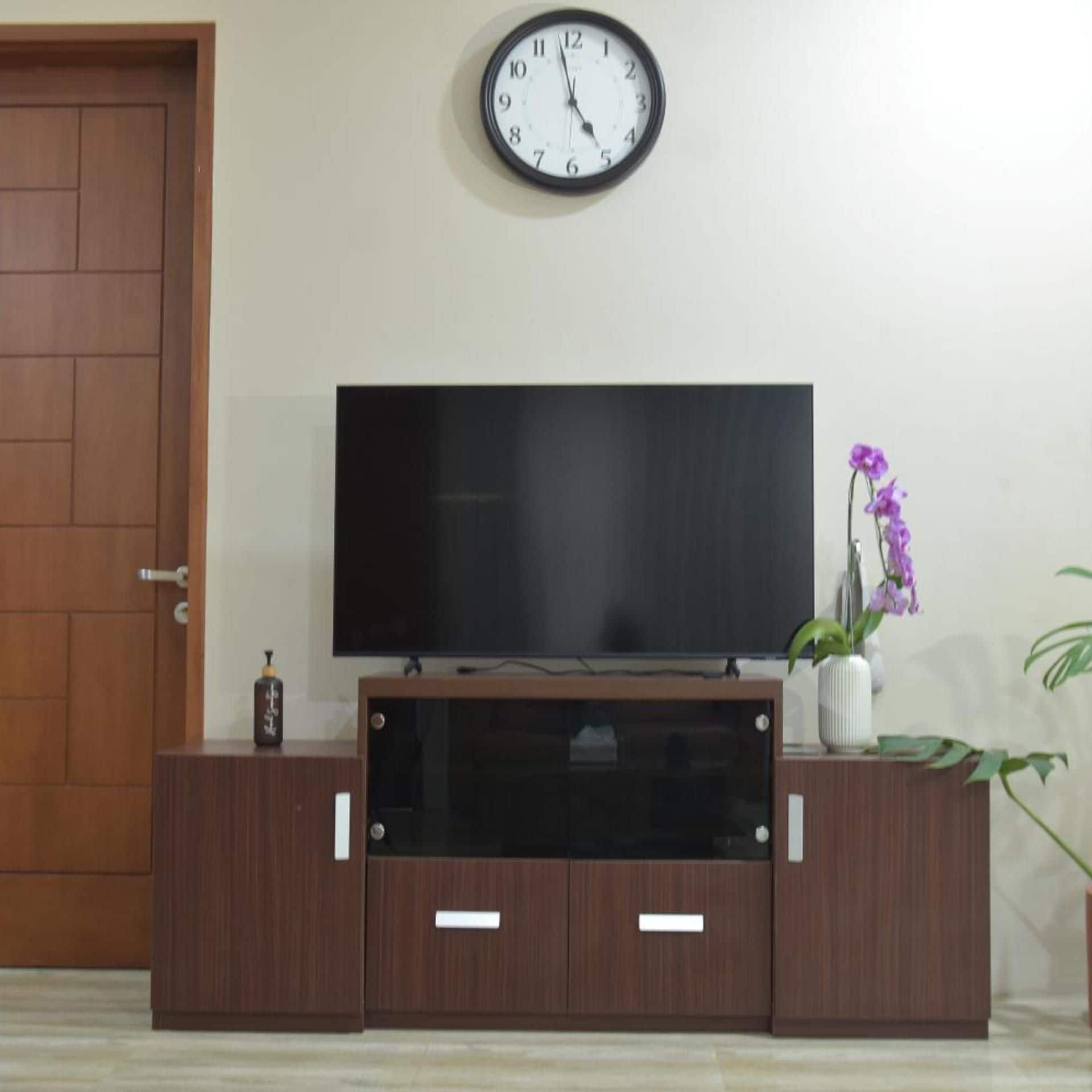A flat-screen TV on a wooden entertainment unit with a clock above it.