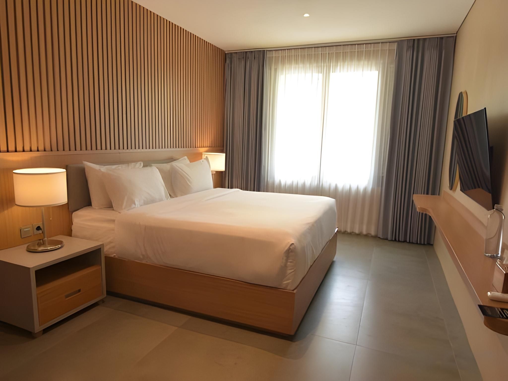 A hotel room with a large bed, bedside tables, a TV, and a window with curtains.