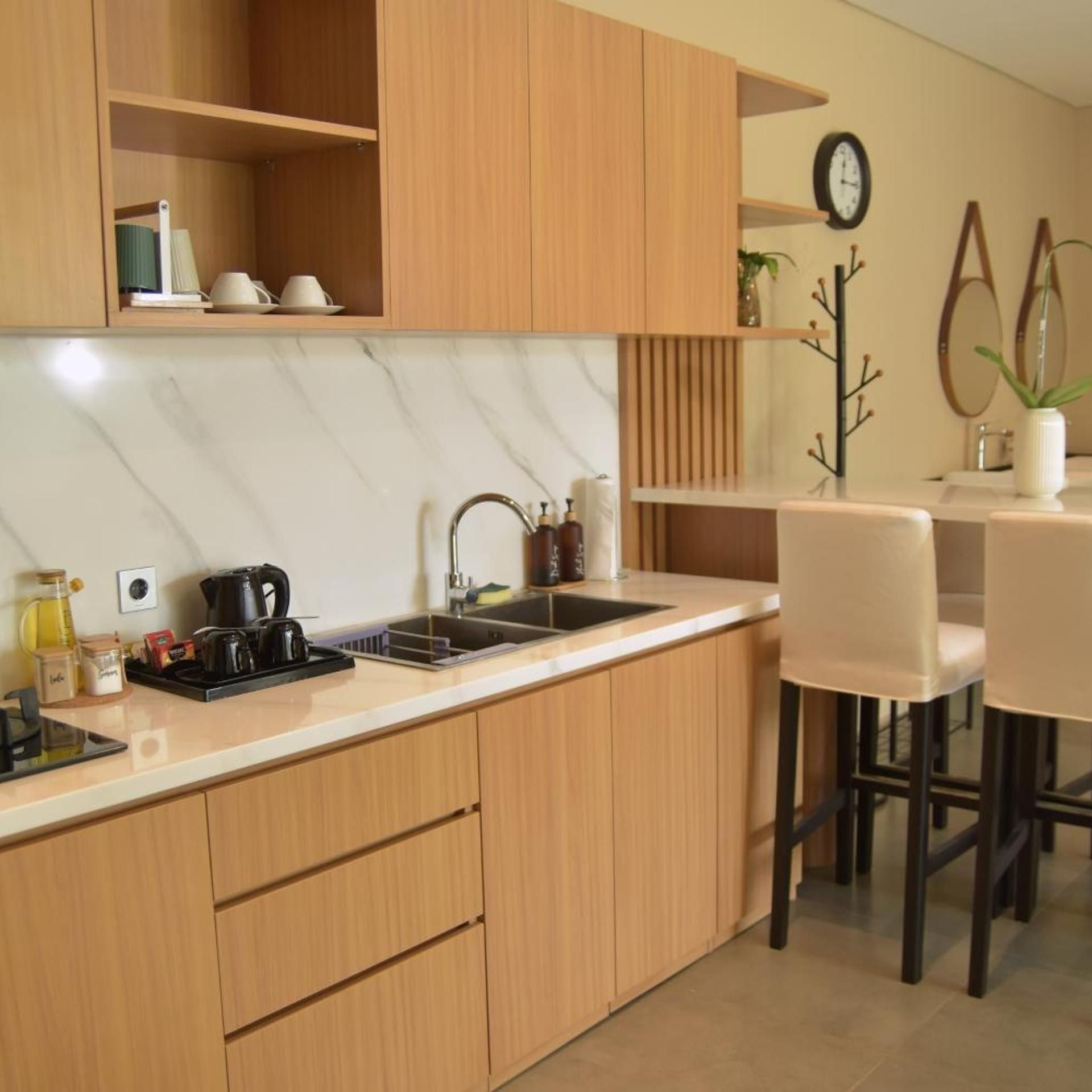 Een moderne keuken met houten kastjes, een marmeren aanrechtblad en een eethoek met een witte tafel en stoelen.